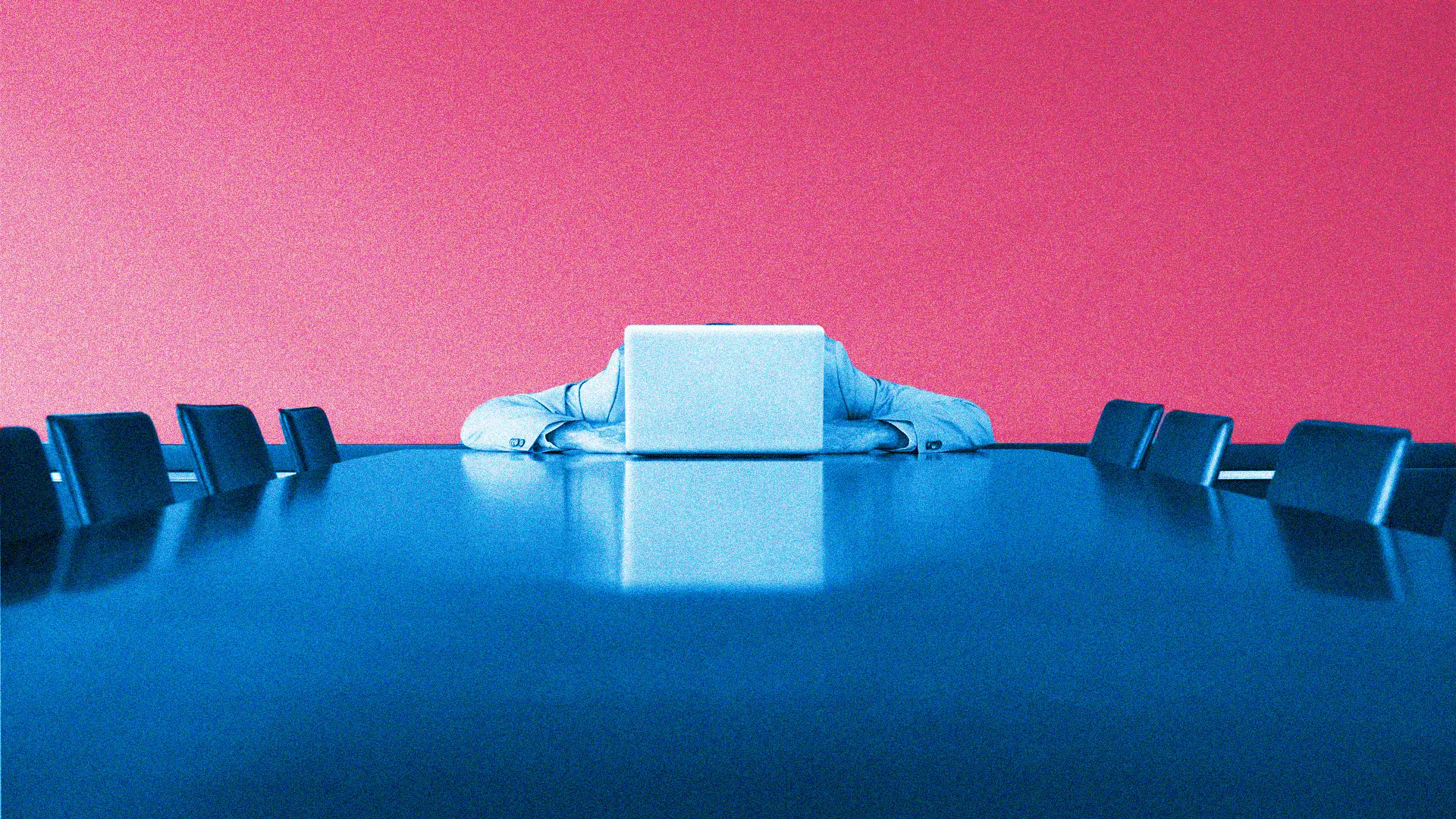 Person with a laptop in front of their face sits at a long conference table, pink wall behind them, blue lighting.